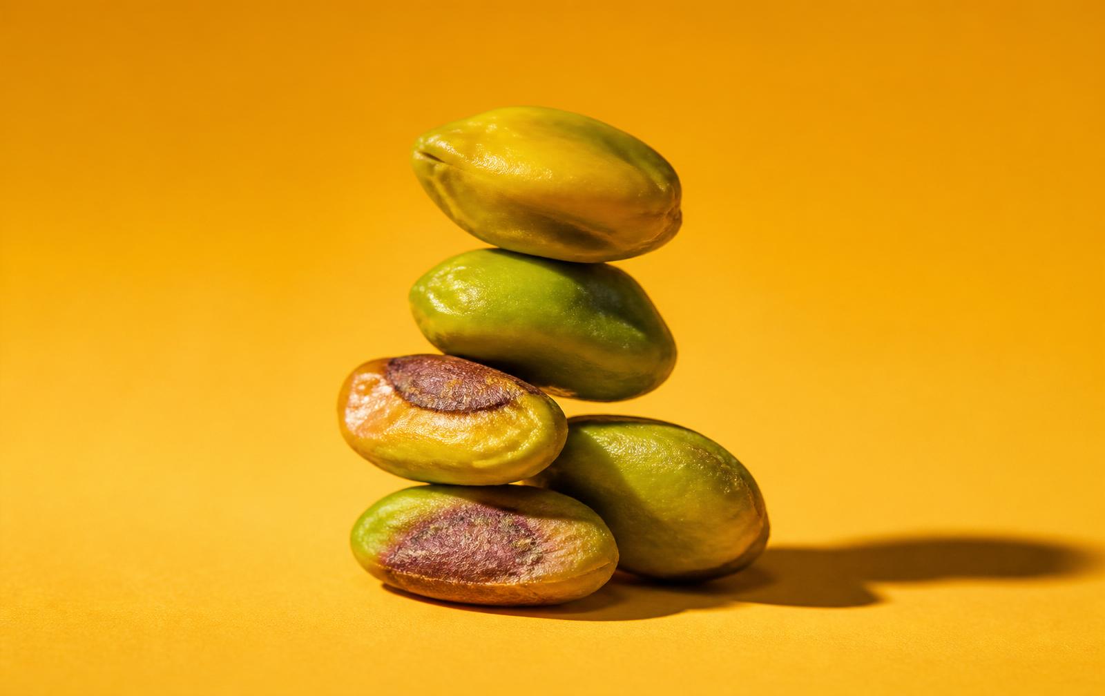 A sculptural stack of shell-free pistachio kernels on a honey-yellow backdrop