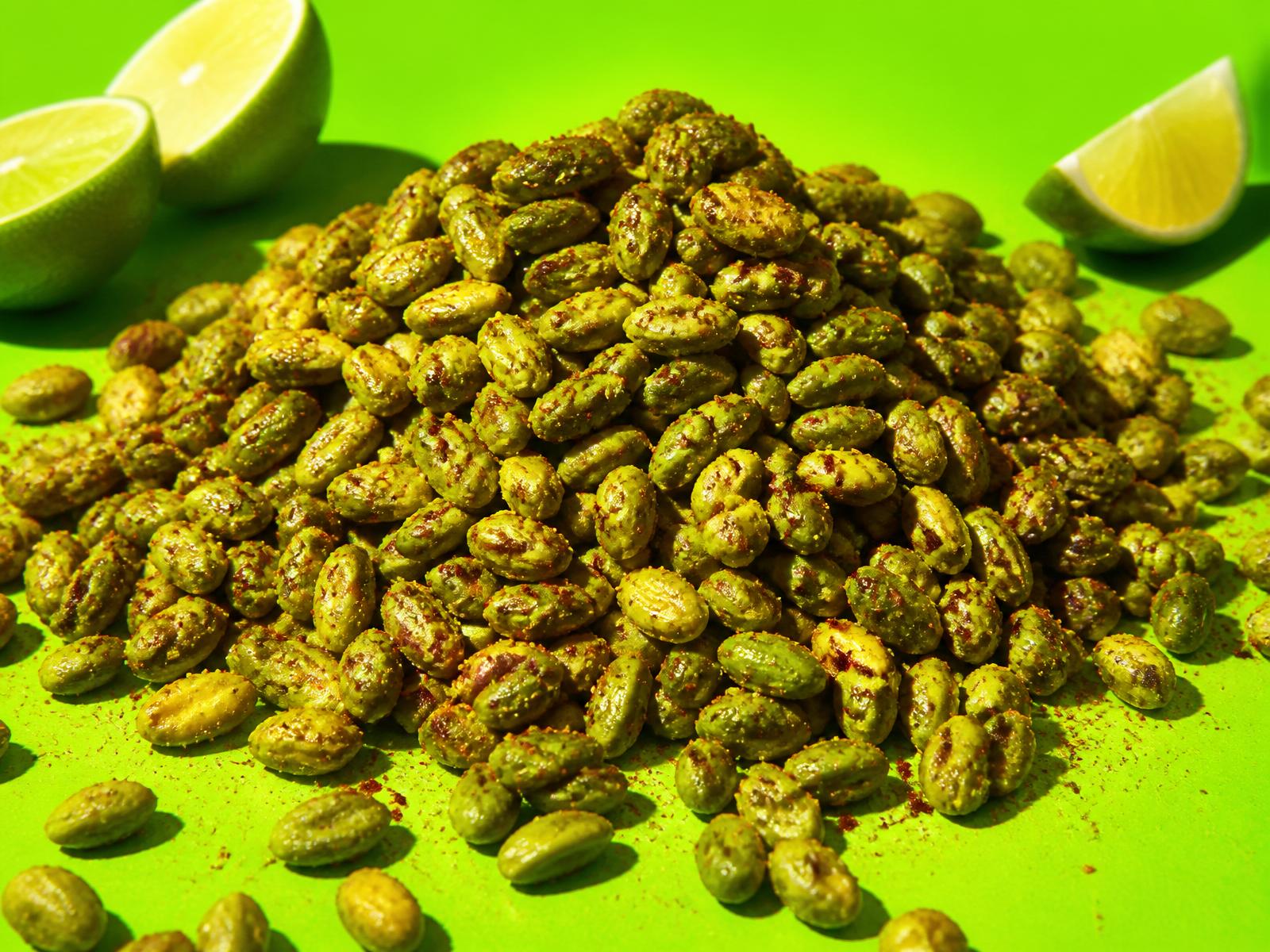 A pile of chili-lime seasoned pistachio kernels with no shells on a bright green backdrop