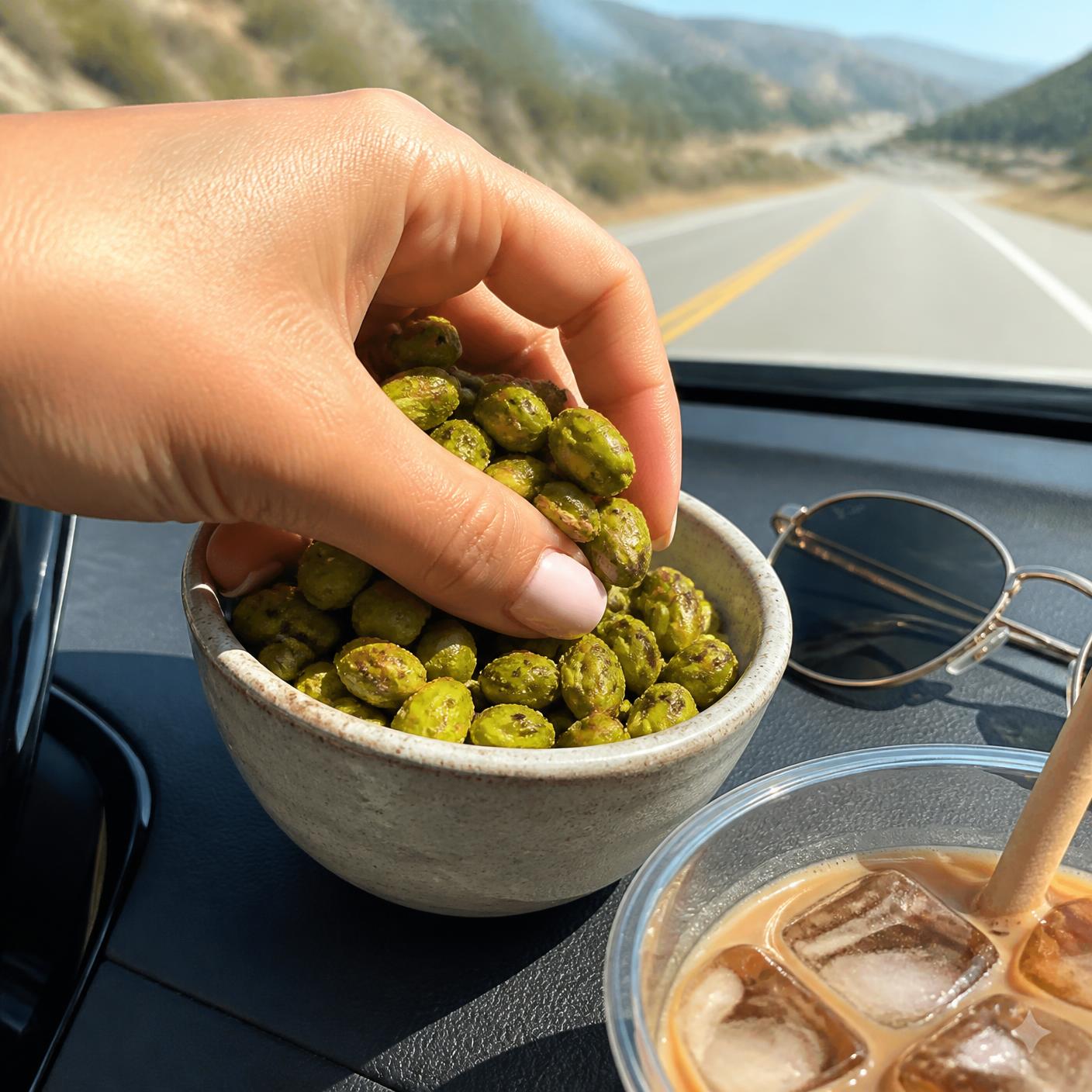 A hand grabbing seasoned shell-free pistachio kernels from a bowl on a car dashboard